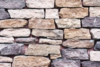 Rustik mur av oregelbundna naturstenblock i varierande färger.